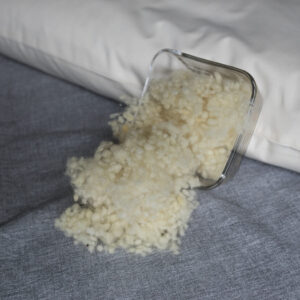 Schafswolle in Glasschüssel an ein Körnerkopfkissen angelehnt. Schafswollefüllung für Körnerkopfkissen.