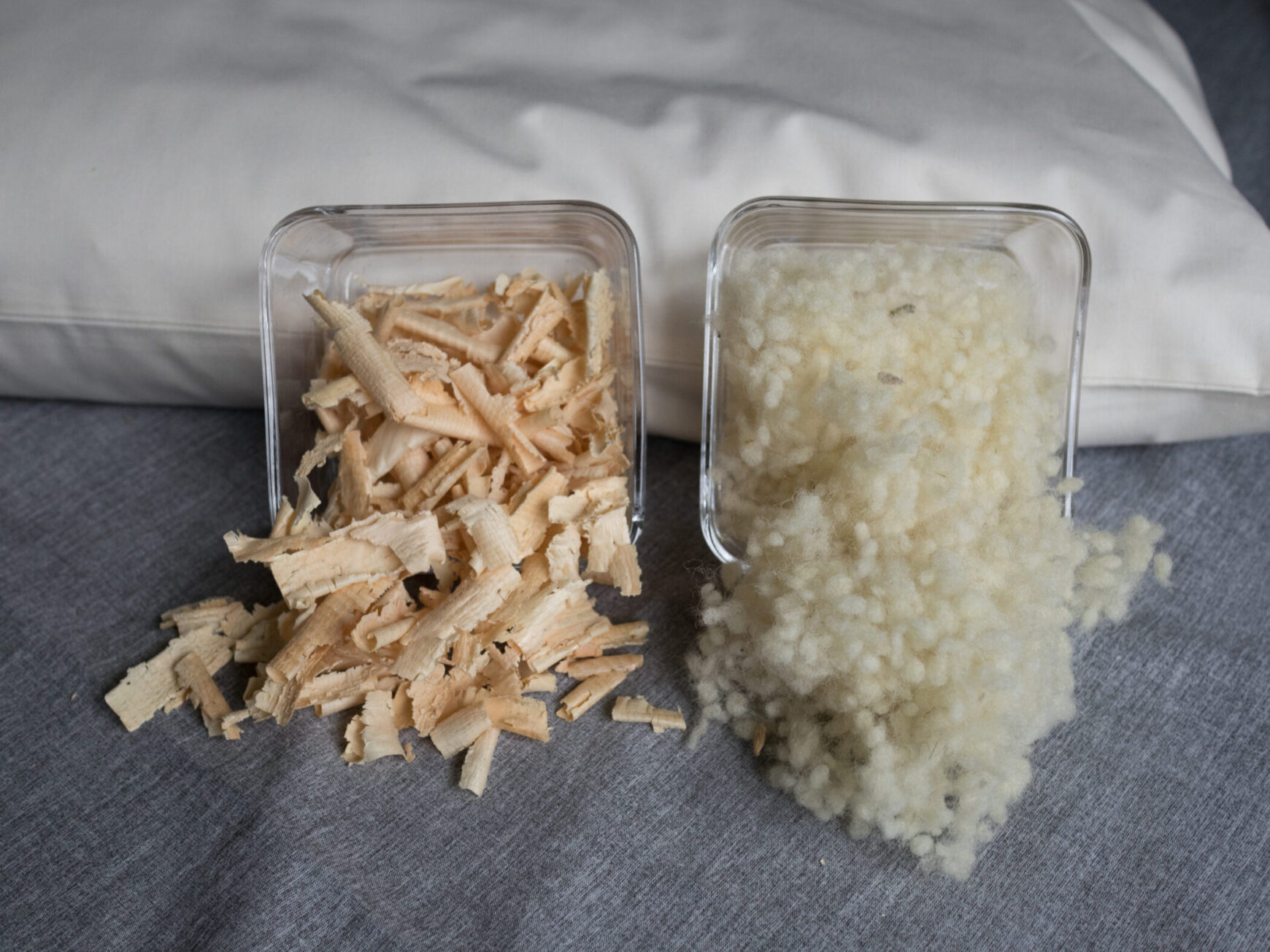 Schafswolle und Zirbenspäne in Glasschüsseln an ein Körnerkopfkissen angelehnt. Schafswollefüllung und Zirbenfüllung für Körnerkopfkissen.
